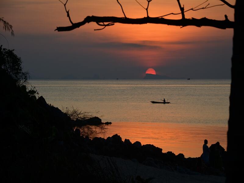 rocks, tree, person, and boat in silhouette against a setting sun