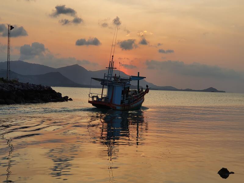 Fishing boat at sea against orange, yellow, and purple sky