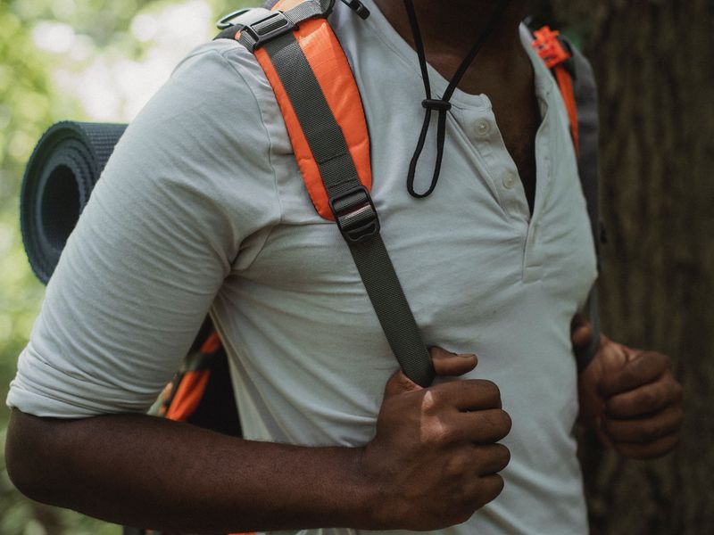 This image shows a man holding the straps of his backpack in a white shirt.