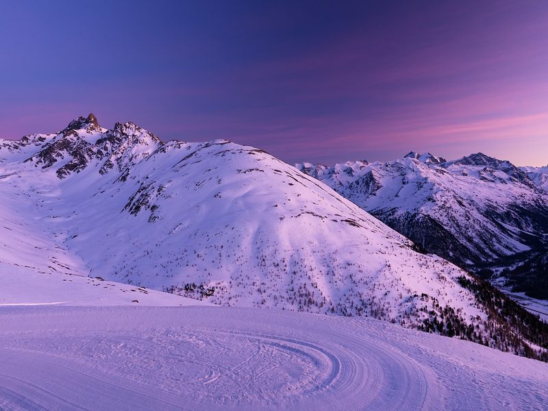This image shows snowy slopes at purple sunrise.